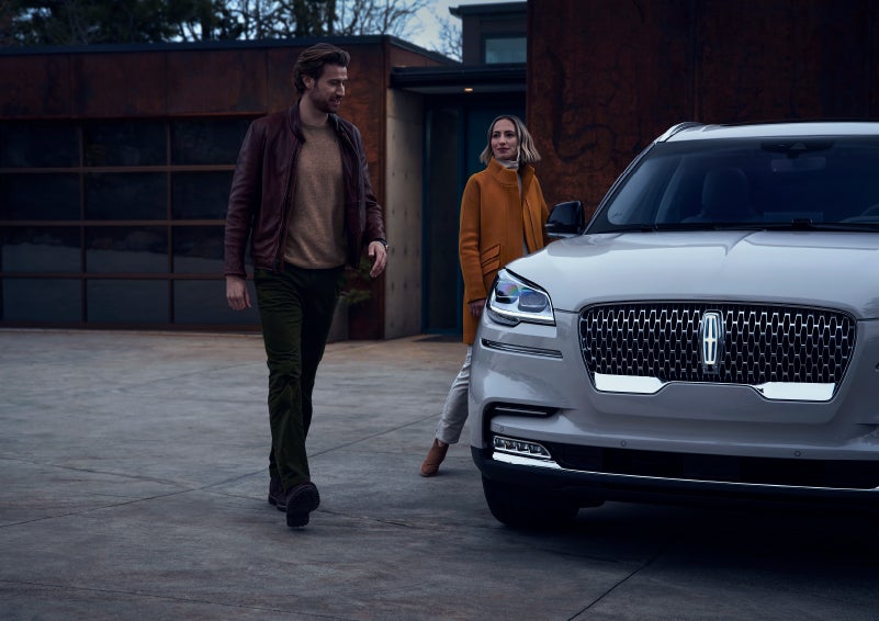 A man and a woman approaching a 2024 Lincoln Aviator® SUV, which illuminates certain lights when they are close | Angela Krause Lincoln of Alpharetta in Alpharetta GA